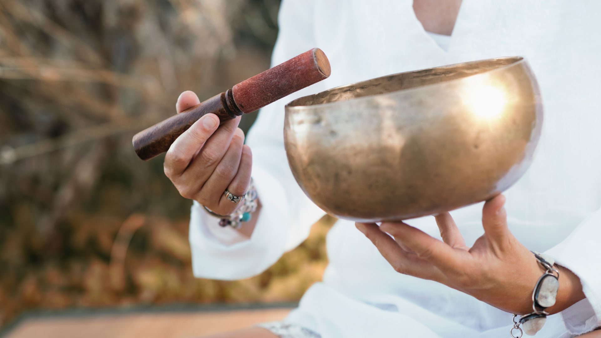 Hands holding a traditional singing bowl and wooden mallet for meditation
